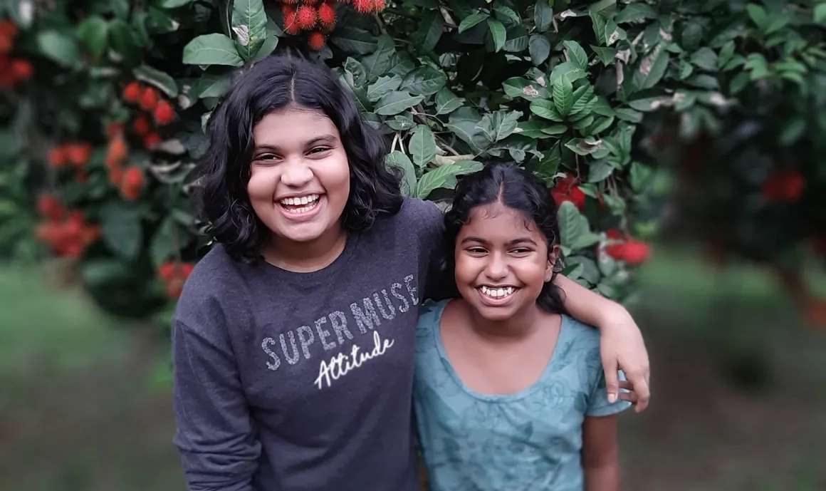 Two girls laughing under a rambutan tree heavy with fruit