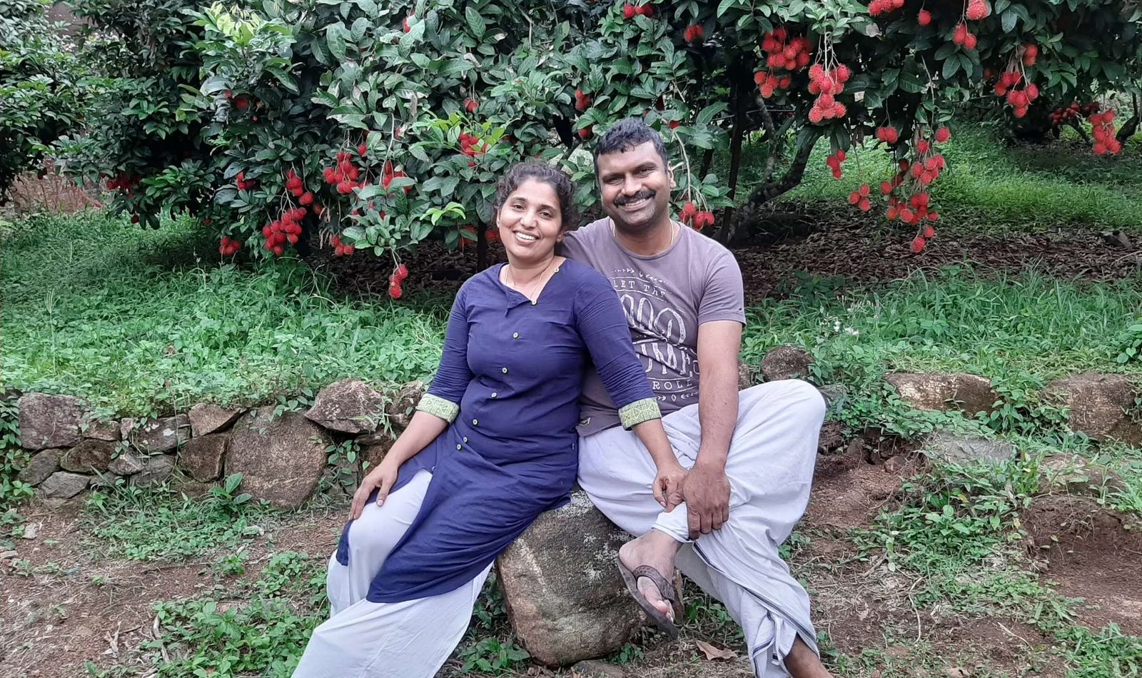 Sandhya and Kurian seated beneath a fruiting rambutan tree