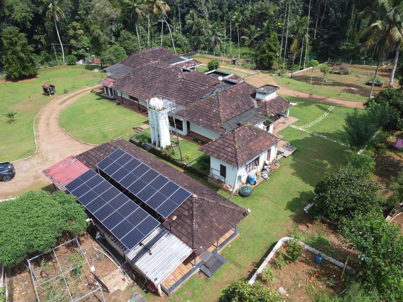 Solar panels on the car shed roof beside the old tiled house, seen from the air